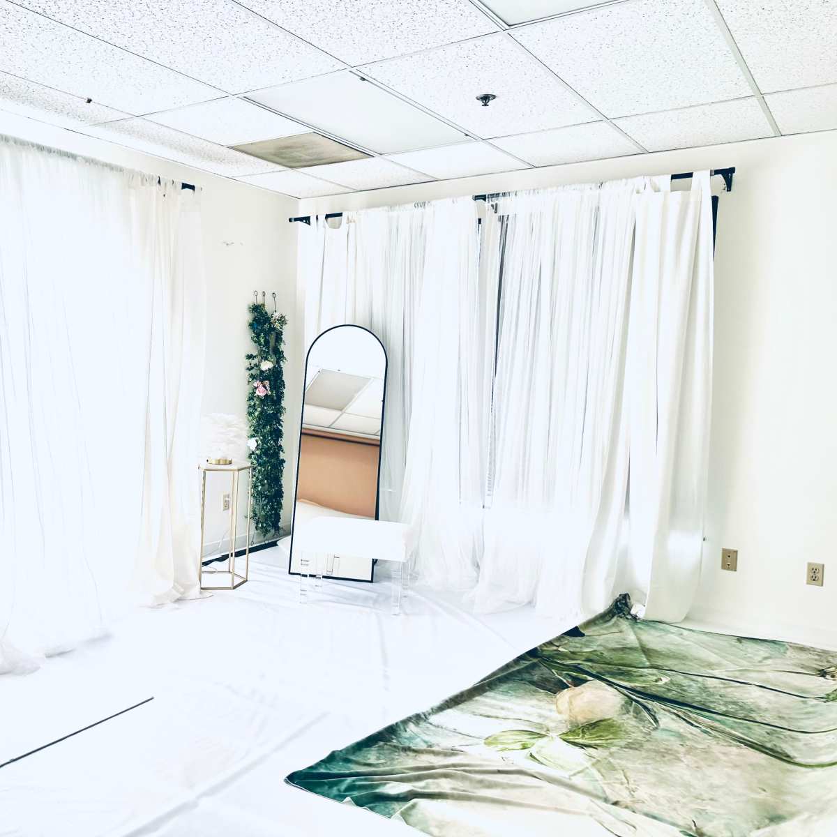 A bright, minimalist room with white curtains, a mirror, and a floor covering featuring a nature scene.