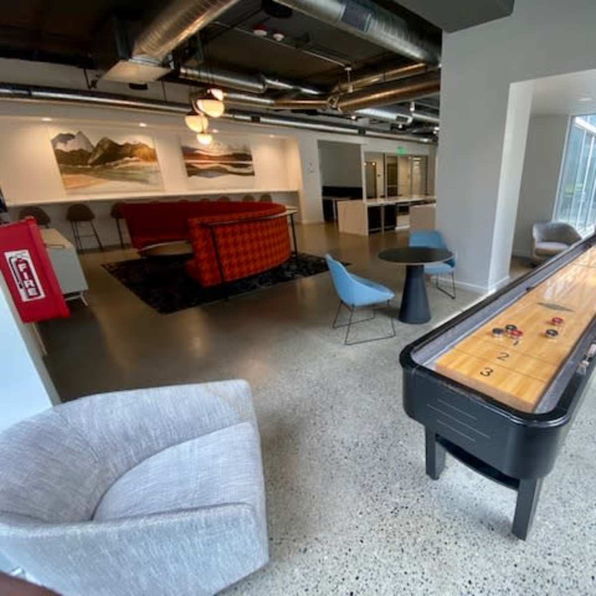 A modern lounge area with a shuffleboard table, comfortable seating, and large windows letting in natural light.
