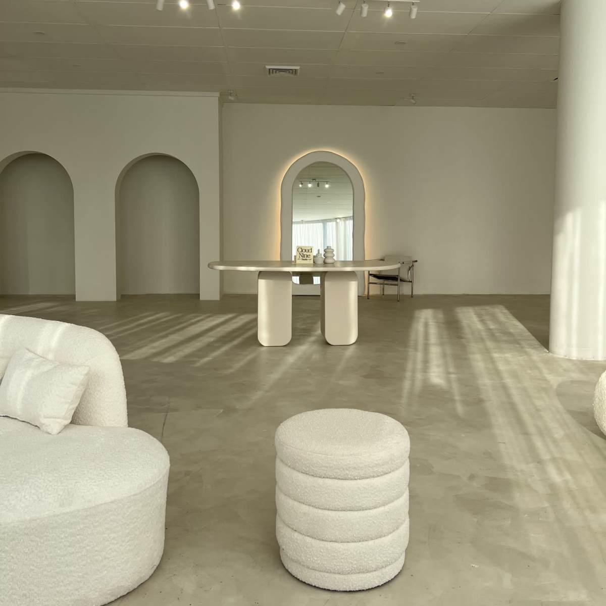 A minimalist interior space with curved arches, a central table, and a mirror reflecting light.