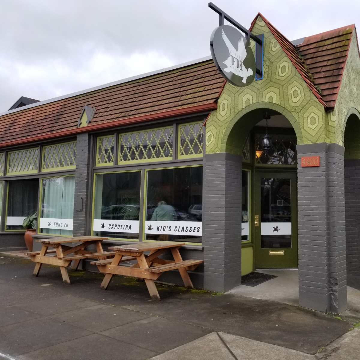 A green and gray restaurant building with large windows and outdoor seating, located at 2400 on the street.