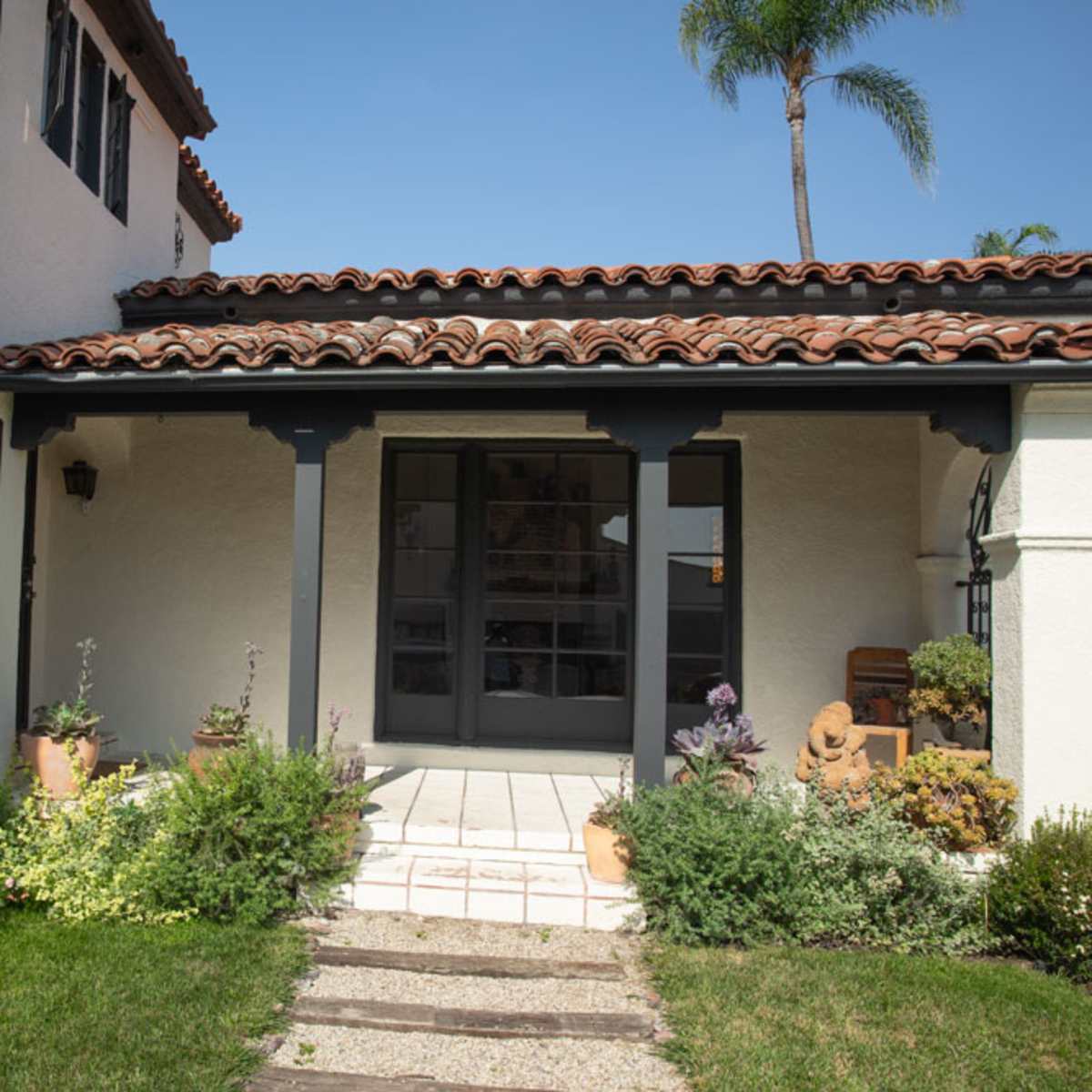 A well-maintained entryway of a house, featuring a tiled path, potted plants, and a wooden door under a tiled roof.
