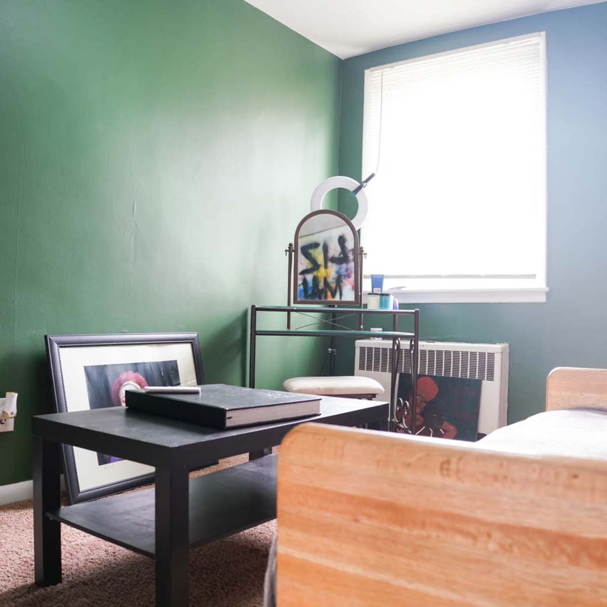 A room features a green wall, a wooden couch, a coffee table, an armchair, and a window with natural light.