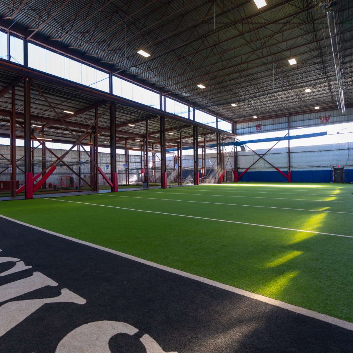 A spacious indoor sports facility with artificial turf and designated training areas.