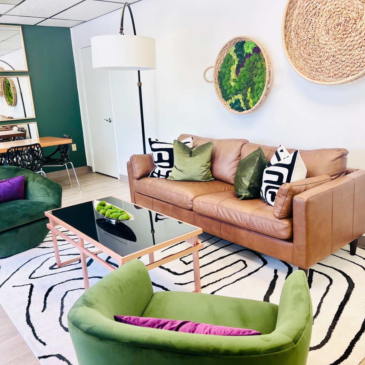 A modern living room featuring a brown leather sofa, two green armchairs, a black coffee table, and decorative wall art.