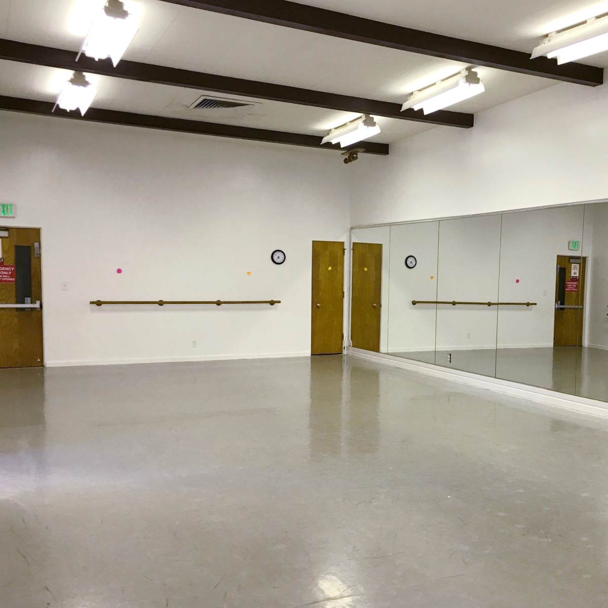 A spacious dance studio with mirrored walls, wooden barre, and two doors.