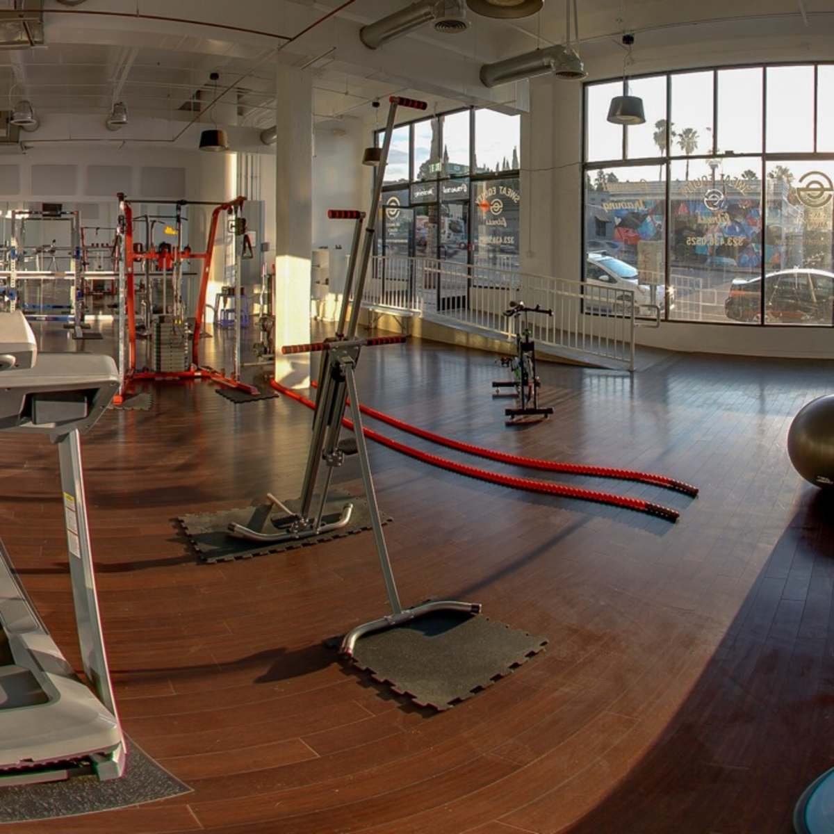 A modern gym interior featuring a treadmill, exercise equipment, and large windows allowing natural light to fill the space.