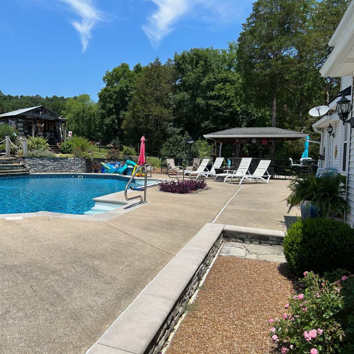 A residential backyard with a swimming pool, lounge chairs, and a gazebo surrounded by greenery.
