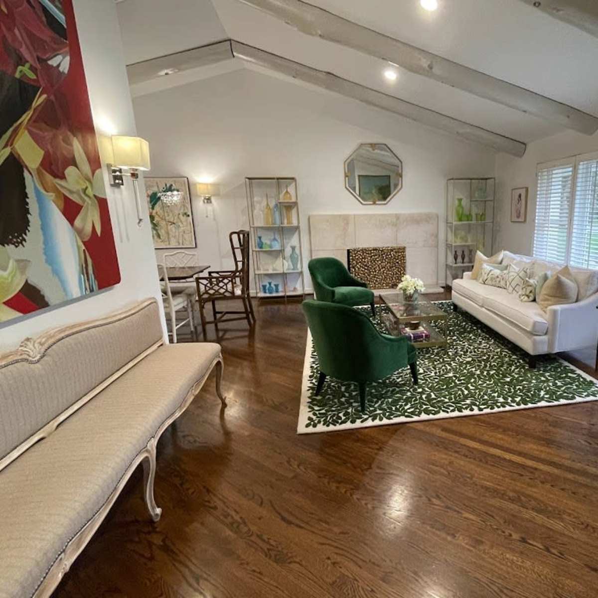 A modern living room features a white sofa, green armchairs, and a decorative rug, with large windows and wooden beams adding to the airy atmosphere.