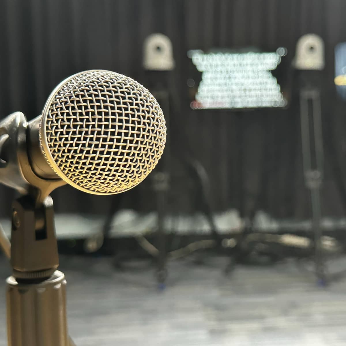 A microphone is positioned in the foreground with blurred screens and equipment in the background.
