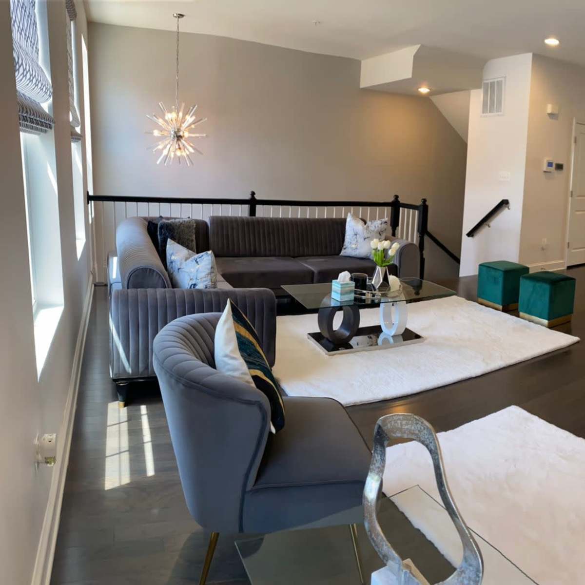 A spacious living room with modern furniture, including a sectional couch and armchairs, leading to an open kitchen area with bar seating.