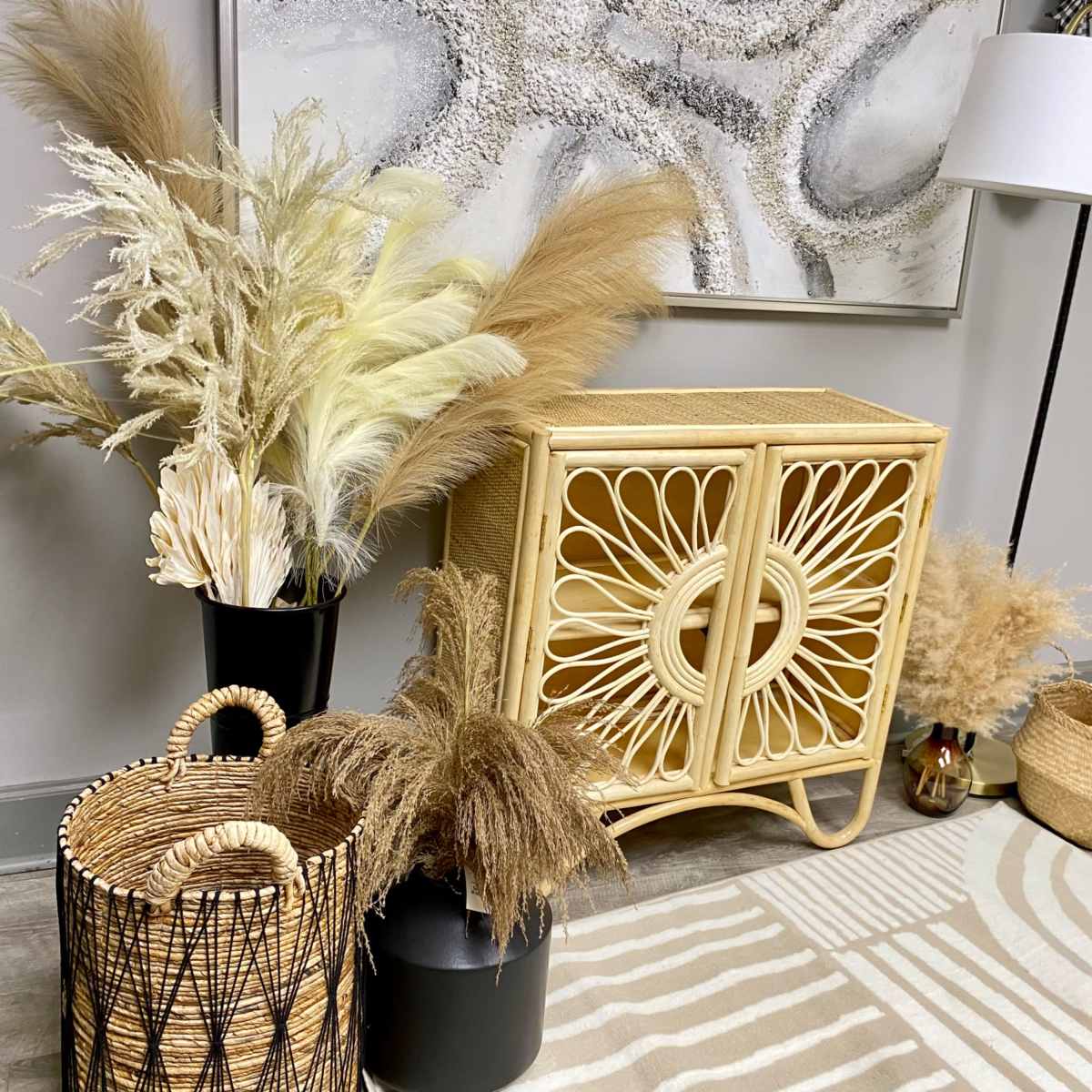 A rattan cabinet with decorative patterns is surrounded by various dried plants and woven baskets in a neutral-toned room.