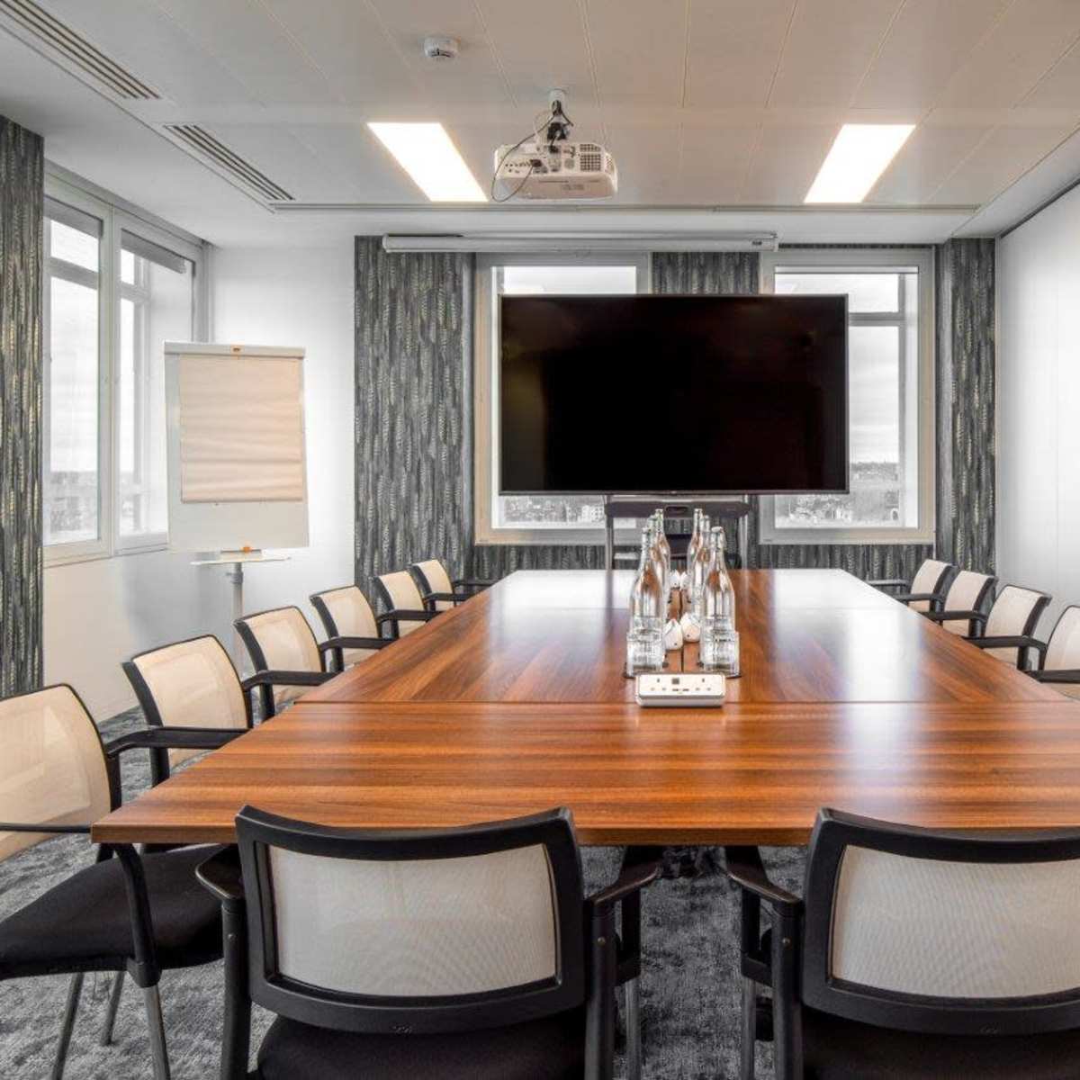 A large conference room features a wooden table surrounded by chairs, a projector, and a large screen on the wall.