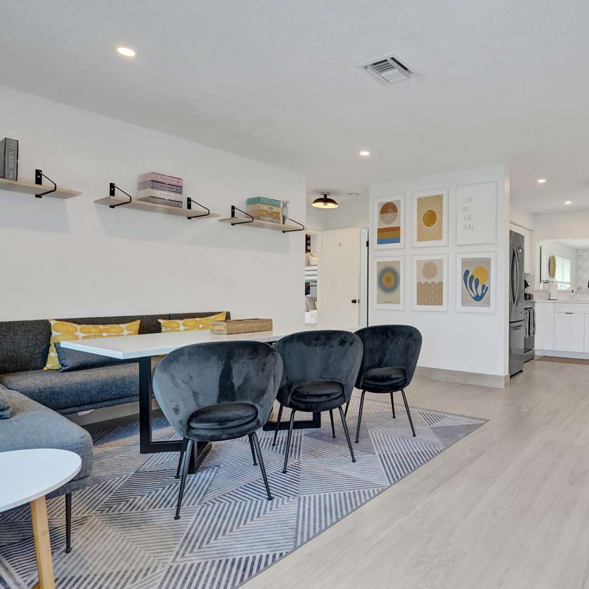 A modern, open-concept living and dining area with a sectional sofa, a round coffee table, a rectangular dining table with chairs, and a kitchen in the background.