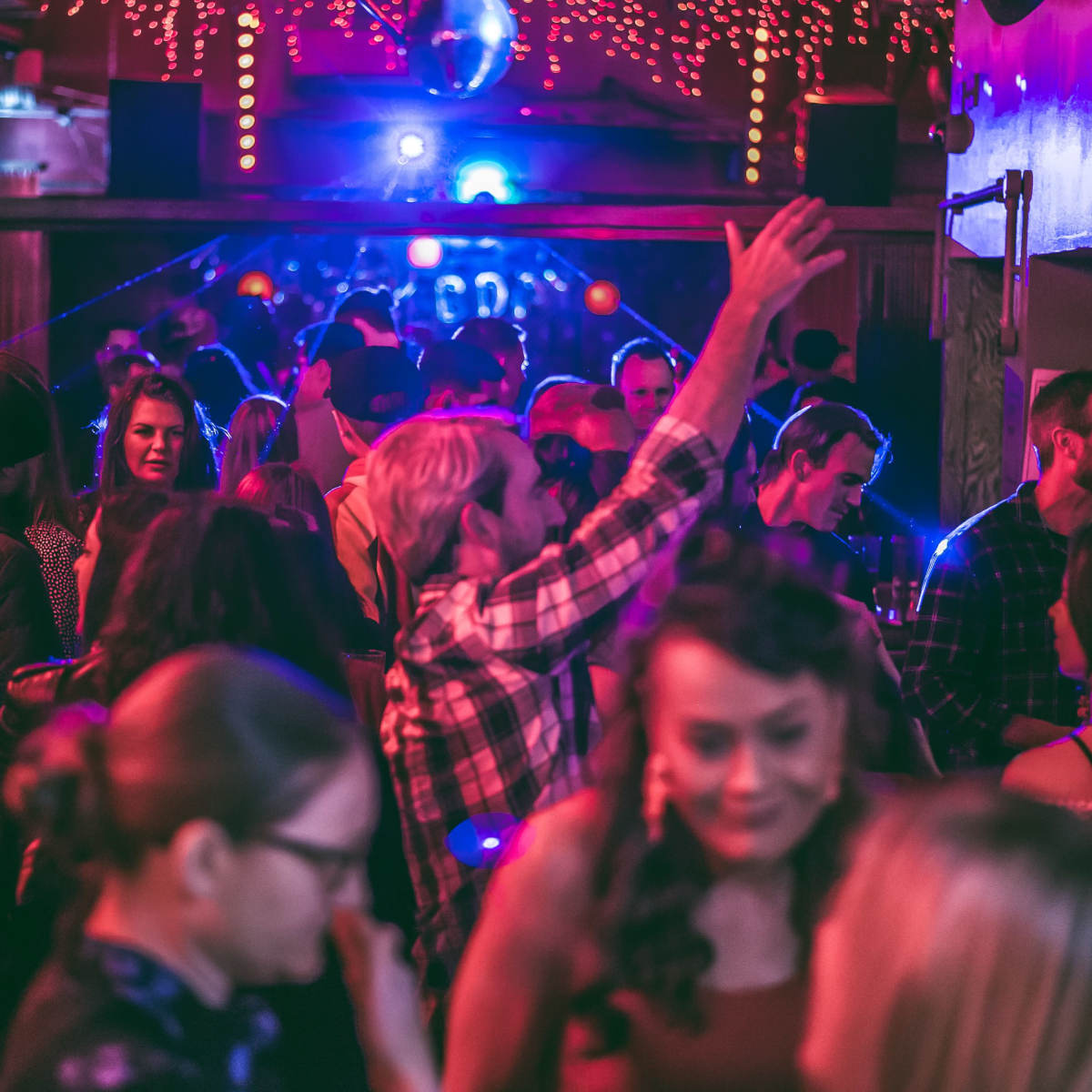 A crowded dance floor filled with people enjoying a lively party under colorful lights.