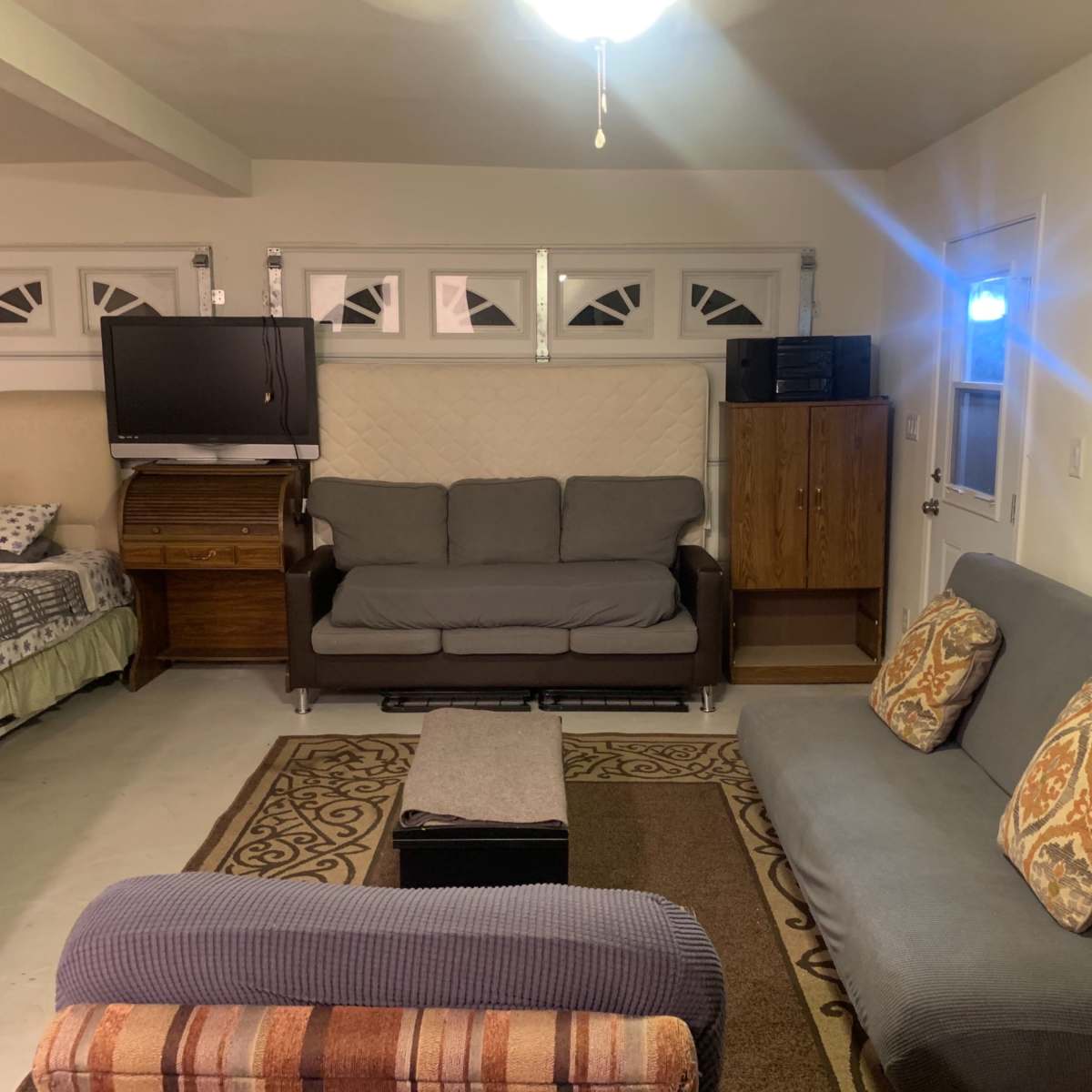 A living room with two sofas, a coffee table, a television, and a doorway leading to another room, all arranged against a backdrop of light-colored walls and a ceiling fan.
