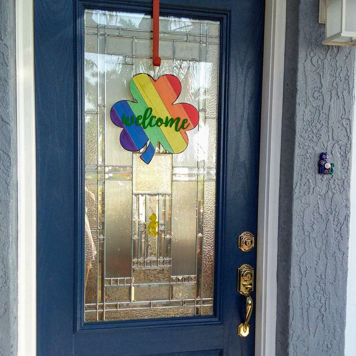 A blue front door with a colorful "welcome" sign shaped like a flower hanging from the top.