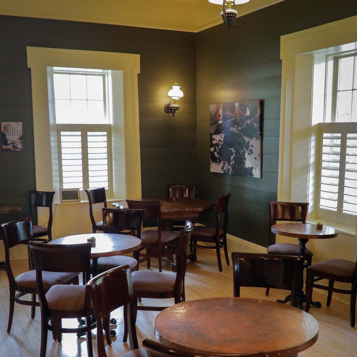 A quiet café interior with several empty wooden tables and chairs arranged in an orderly manner, illuminated by natural light from the windows.