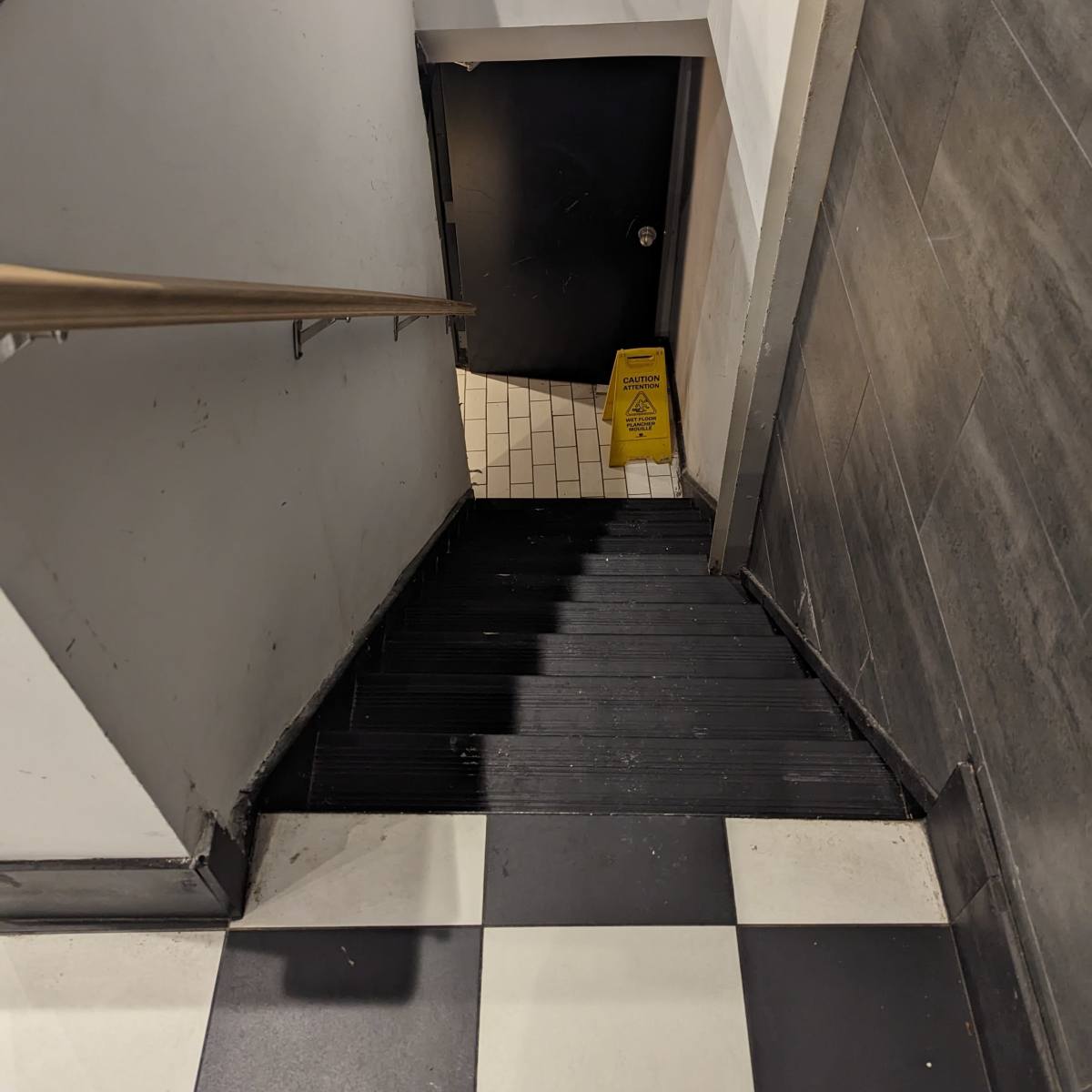 A staircase leads down to a door at the bottom, with a caution sign placed on the landing.