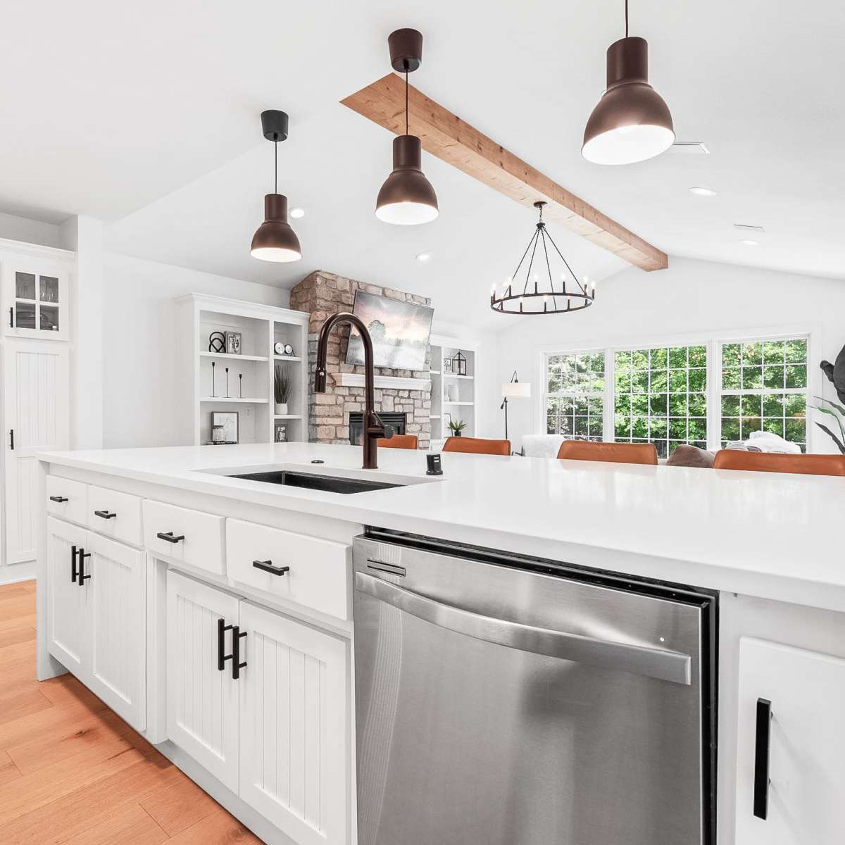 A modern kitchen features white cabinetry, a large island with a stainless steel sink, and a cozy living area visible in the background.