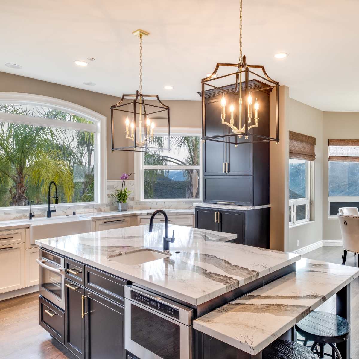 A modern kitchen with a large island featuring marble countertops, pendant lighting, and a dining area with a round table and upholstered chairs.