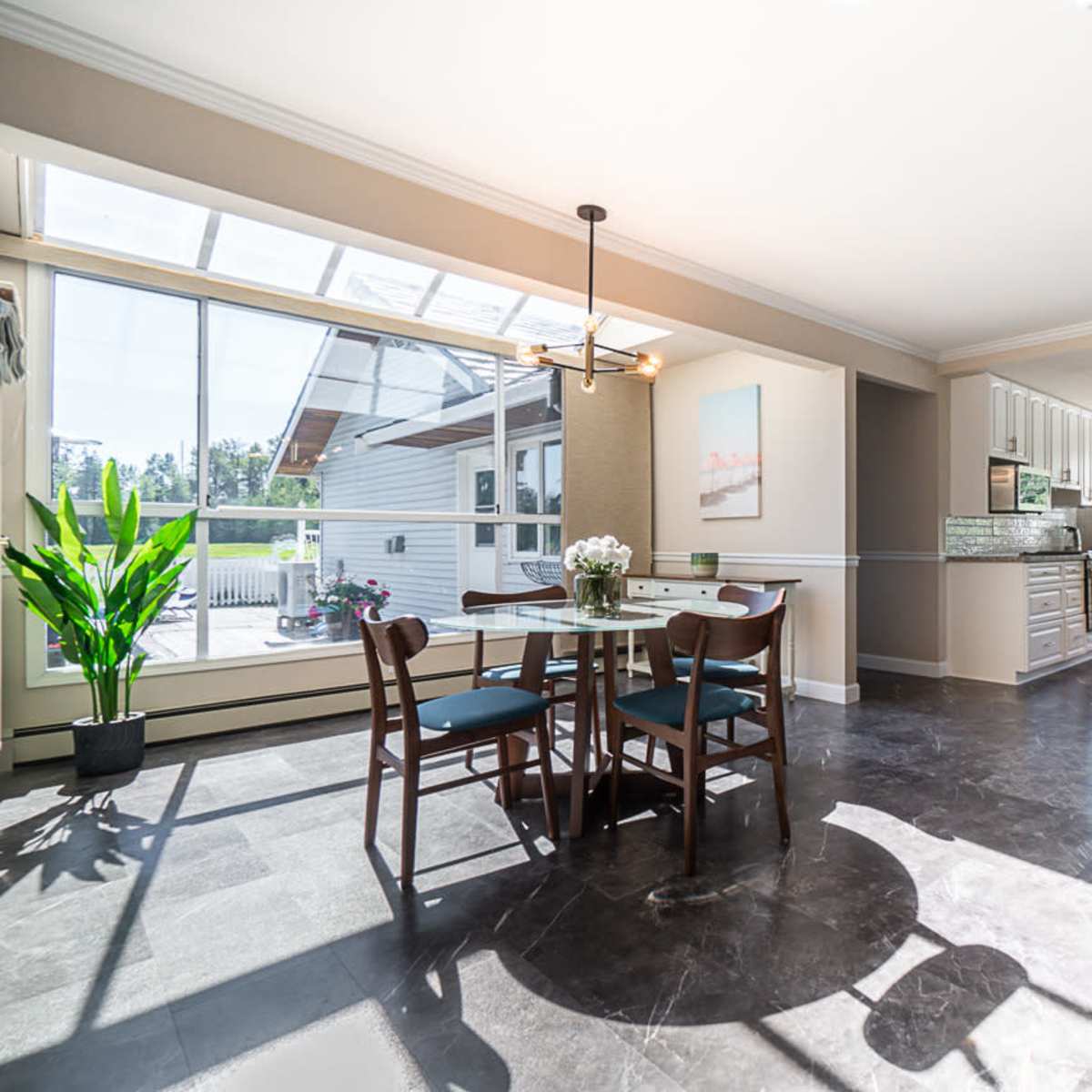 A modern kitchen and dining area with a glass door leading to an outdoor space, featuring a round table with chairs and a bar counter.
