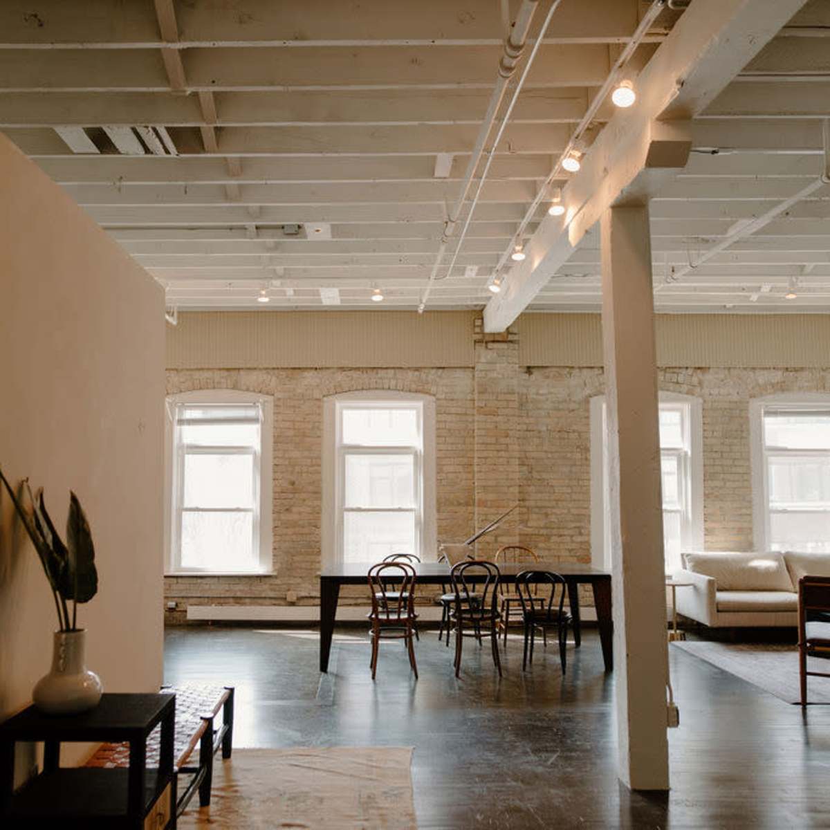 A spacious, minimalist interior of a modern loft with a dining area, living space, and large windows allowing natural light to fill the room.