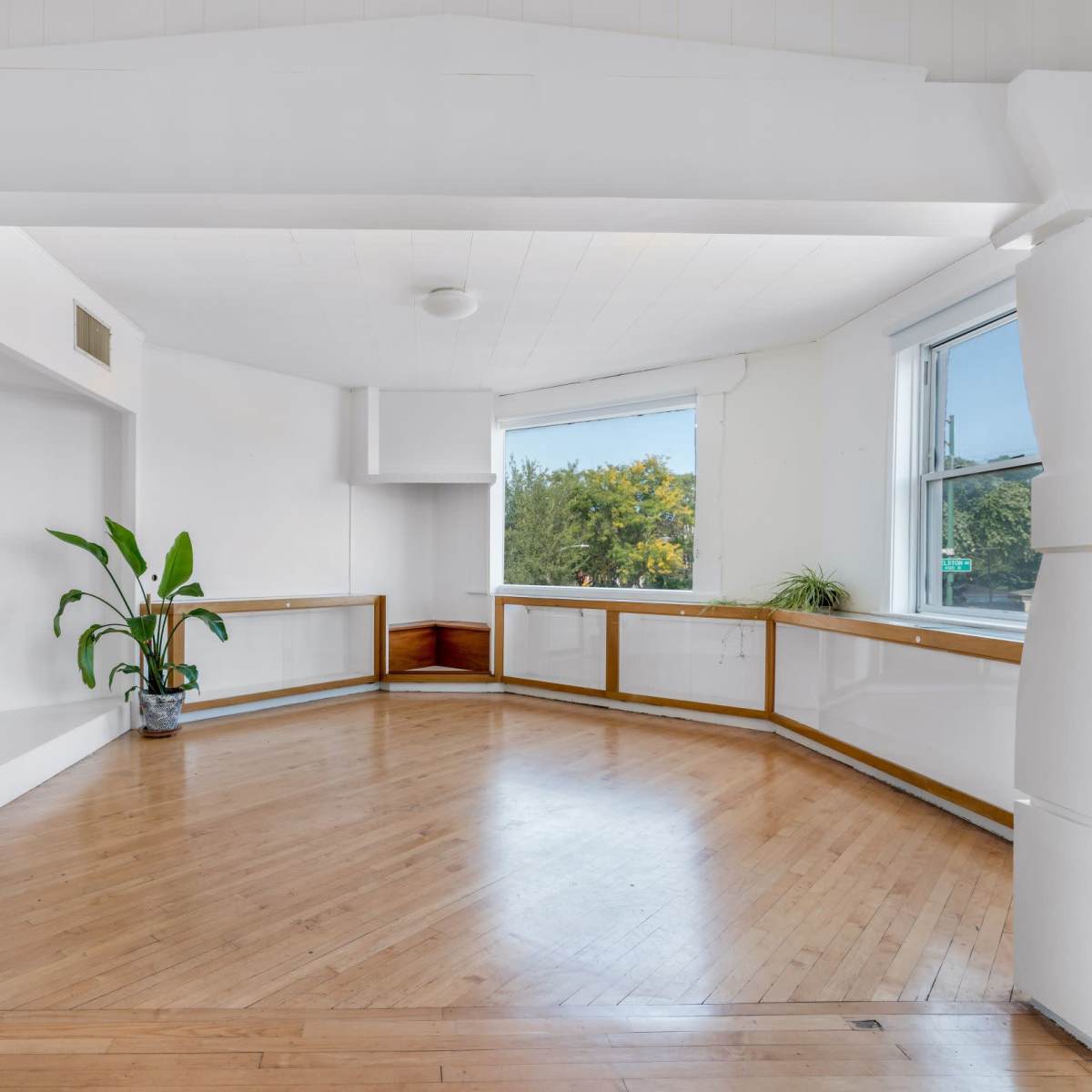 A spacious room features large windows, hardwood flooring, and a curved wall with built-in shelving.
