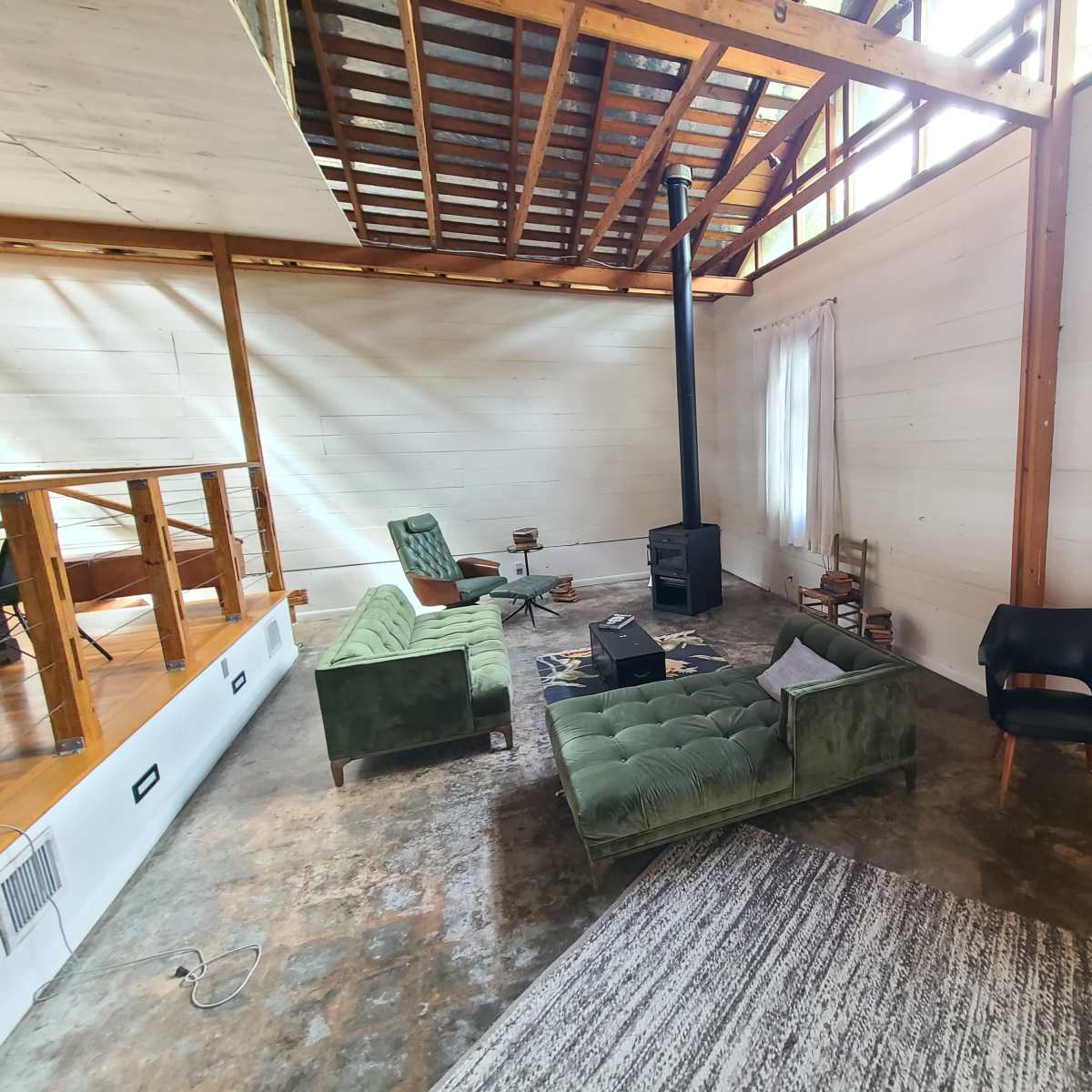 A spacious living area with a black wood stove, green sofas, a black armchair, and a textured rug on the floor.