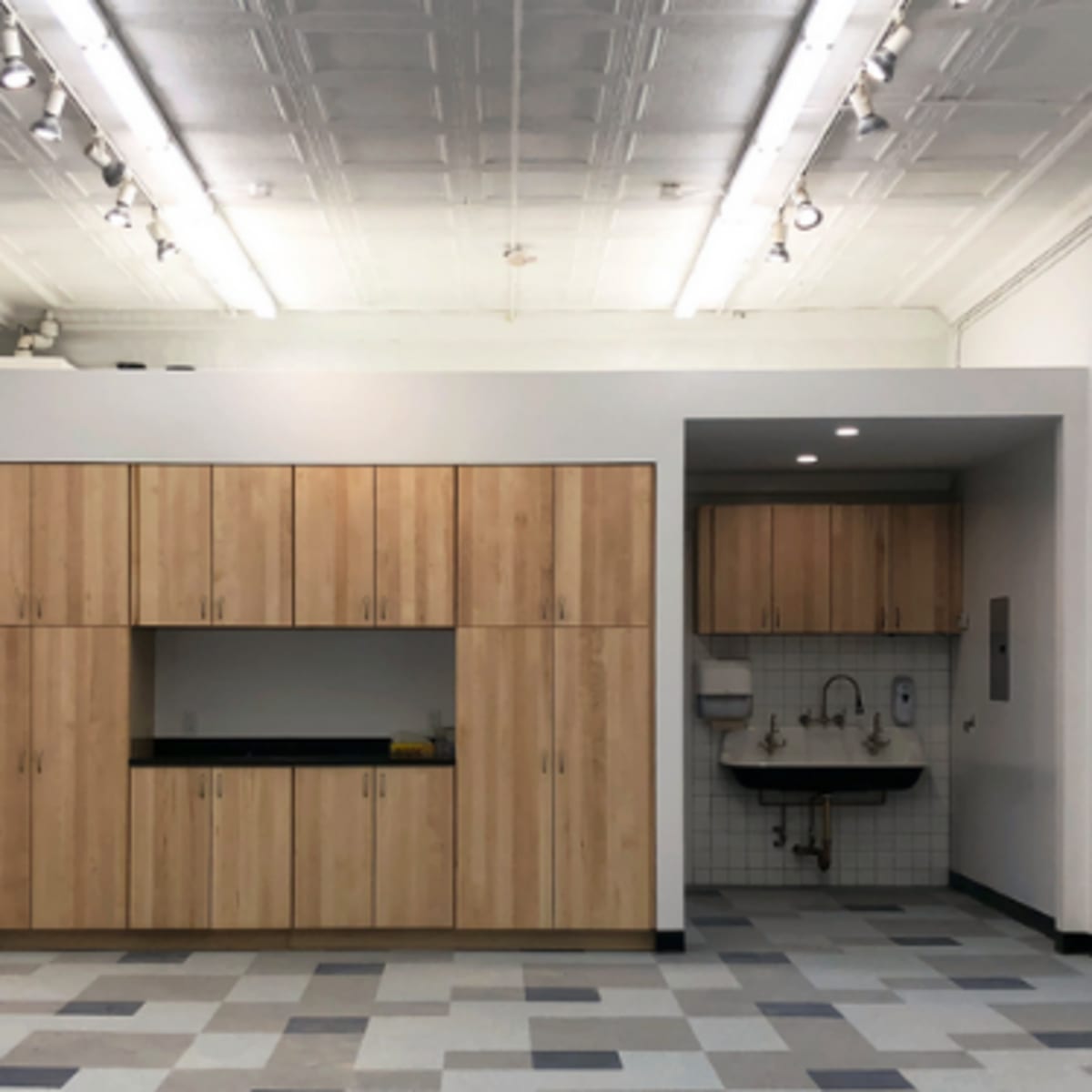 A spacious room with wooden cabinetry and a sink area, featuring a tiled backsplash and a patterned floor.