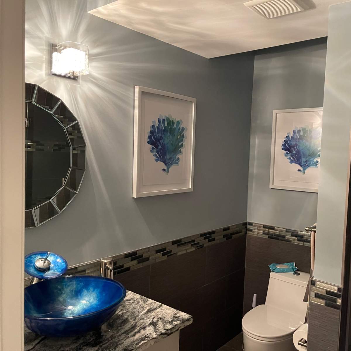A bathroom featuring a round mirror, artistic wall prints, a blue sink, and a shower area.