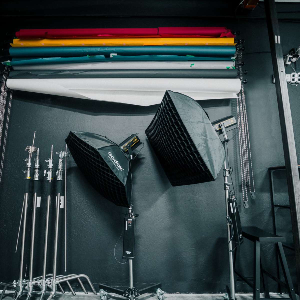 A photography studio with backdrop rolls in various colors hanging on the wall and two softbox lights positioned on stands.