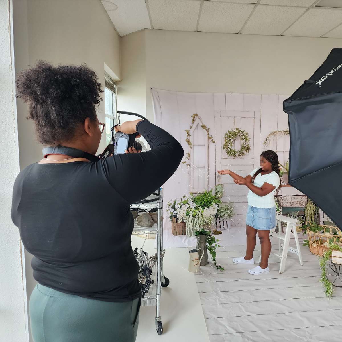 A photographer captures a model posing with greenery in a studio setting adorned with a backdrop and lighting equipment.