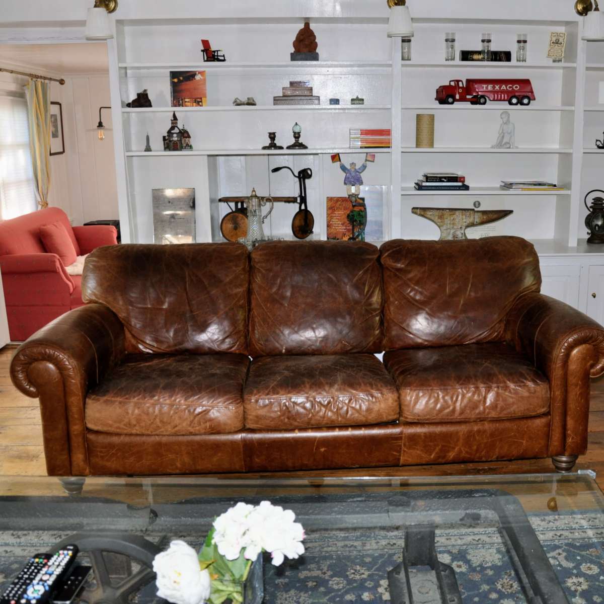 A brown leather sofa in a living room with white shelves displaying various decorative items and a glass coffee table with flowers.