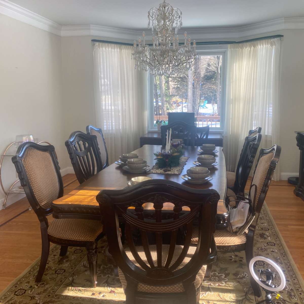 The dining room features a large wooden table set for six, with a chandelier overhead and large windows allowing natural light to fill the space.
