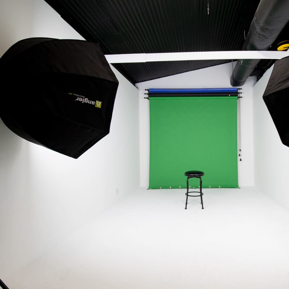 A photography studio with a green backdrop, a black stool in the center, and two large softbox lights on either side.