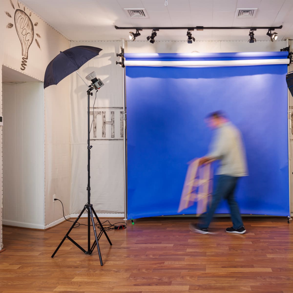 A person is moving a stool in a photography studio with a blue backdrop and lighting equipment set up.