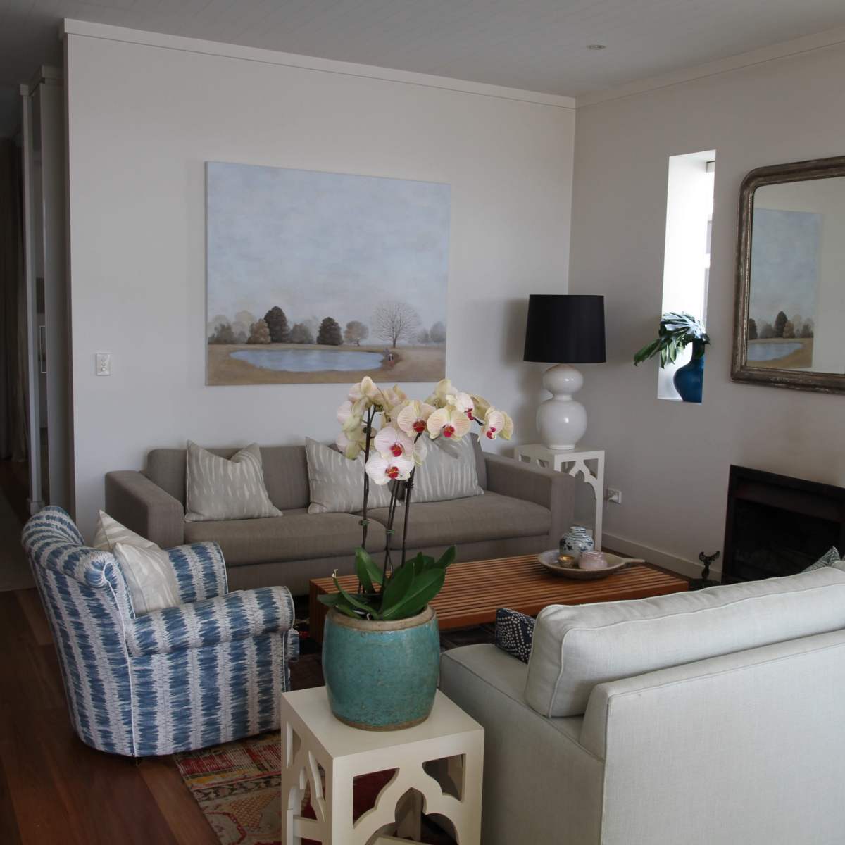 A cozy living room features two sofas, a coffee table, and a large painting, with natural light entering through windows.