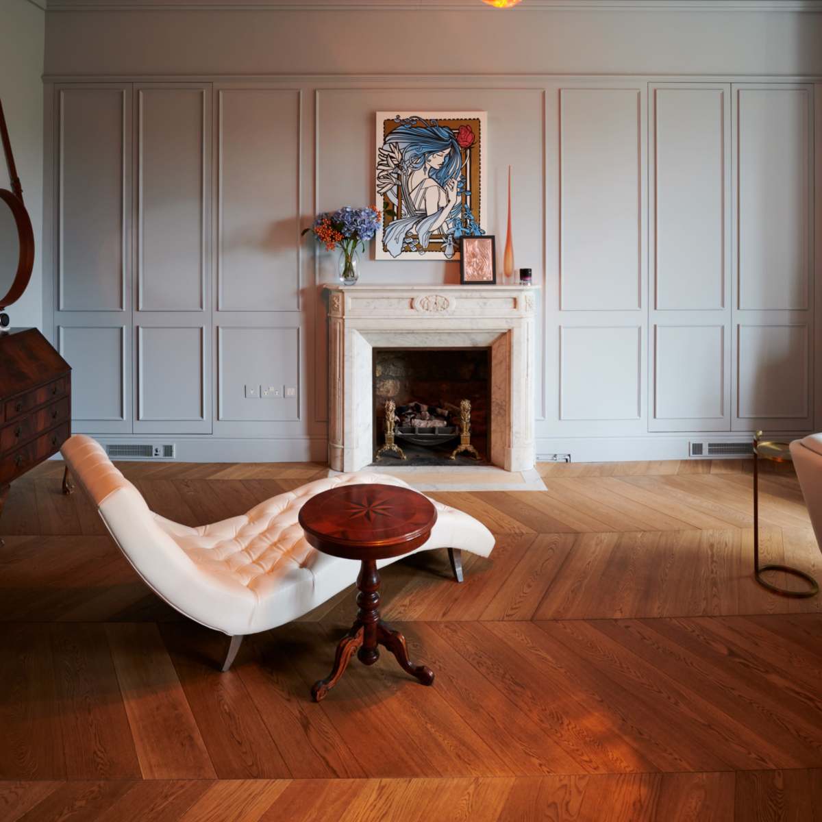 The room features a modern design with a white lounge chair, a small round table, a fireplace with a framed art piece above it, and pendant lights hanging from the ceiling.
