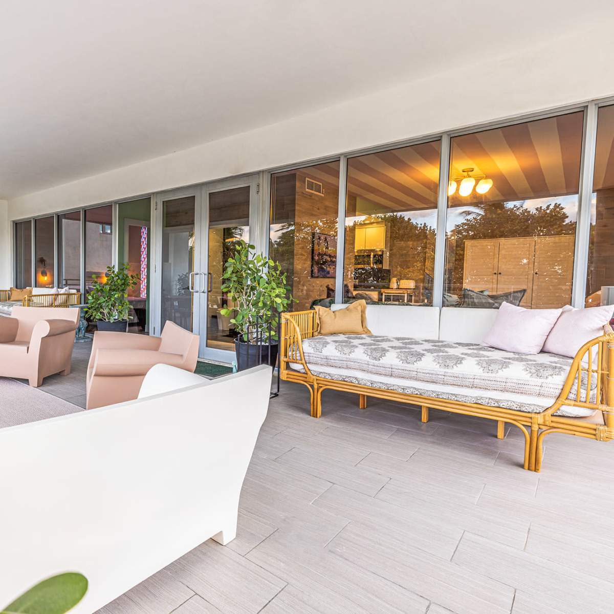 A spacious balcony with modern furniture, including white sofas, a glass table, and potted plants.