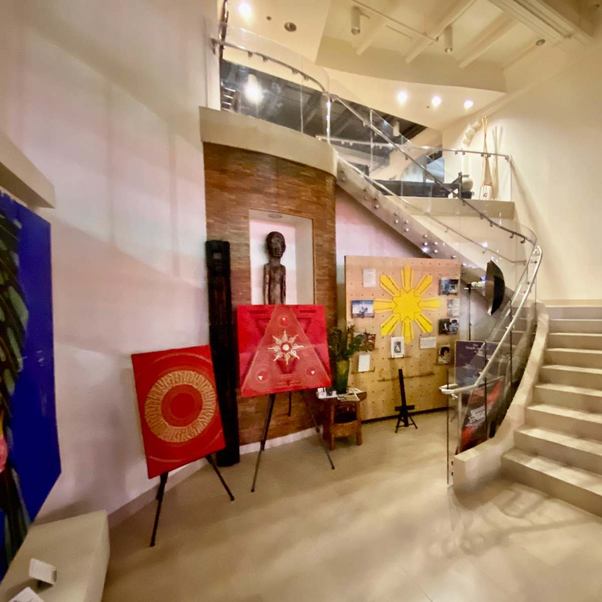 A modern lobby with a staircase leading to an upper level, featuring artwork on the walls and decorative pieces arranged around the space.