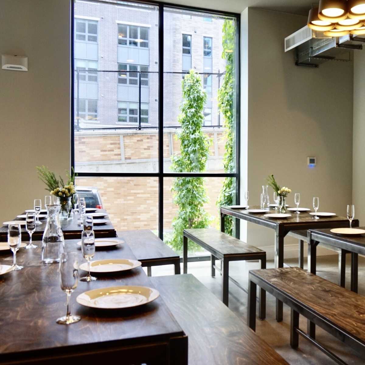 A spacious dining room with wooden tables set for a meal, featuring large windows that allow natural light to enter.