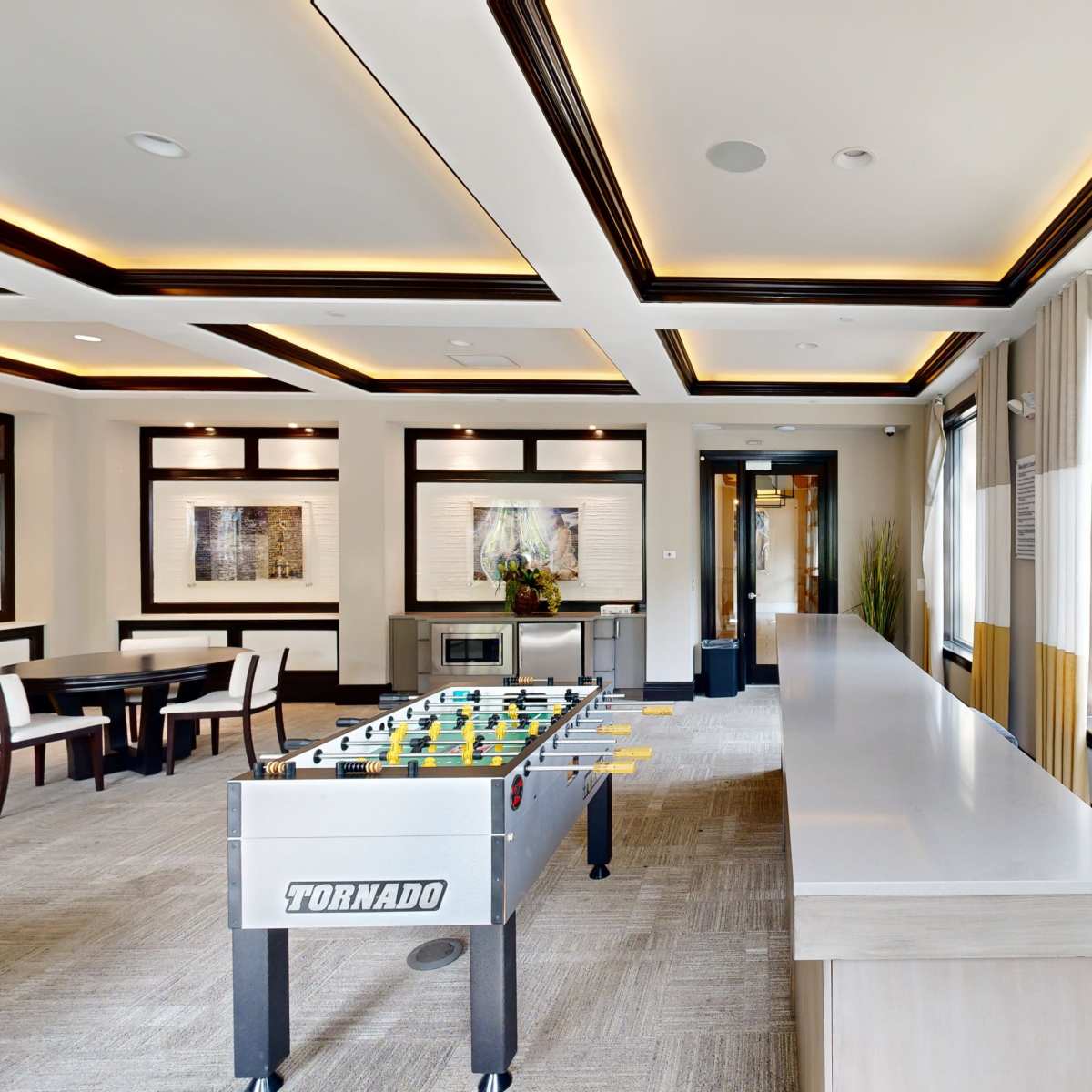 A modern room with a foosball table, large windows, and a bar area featuring a smooth countertop.
