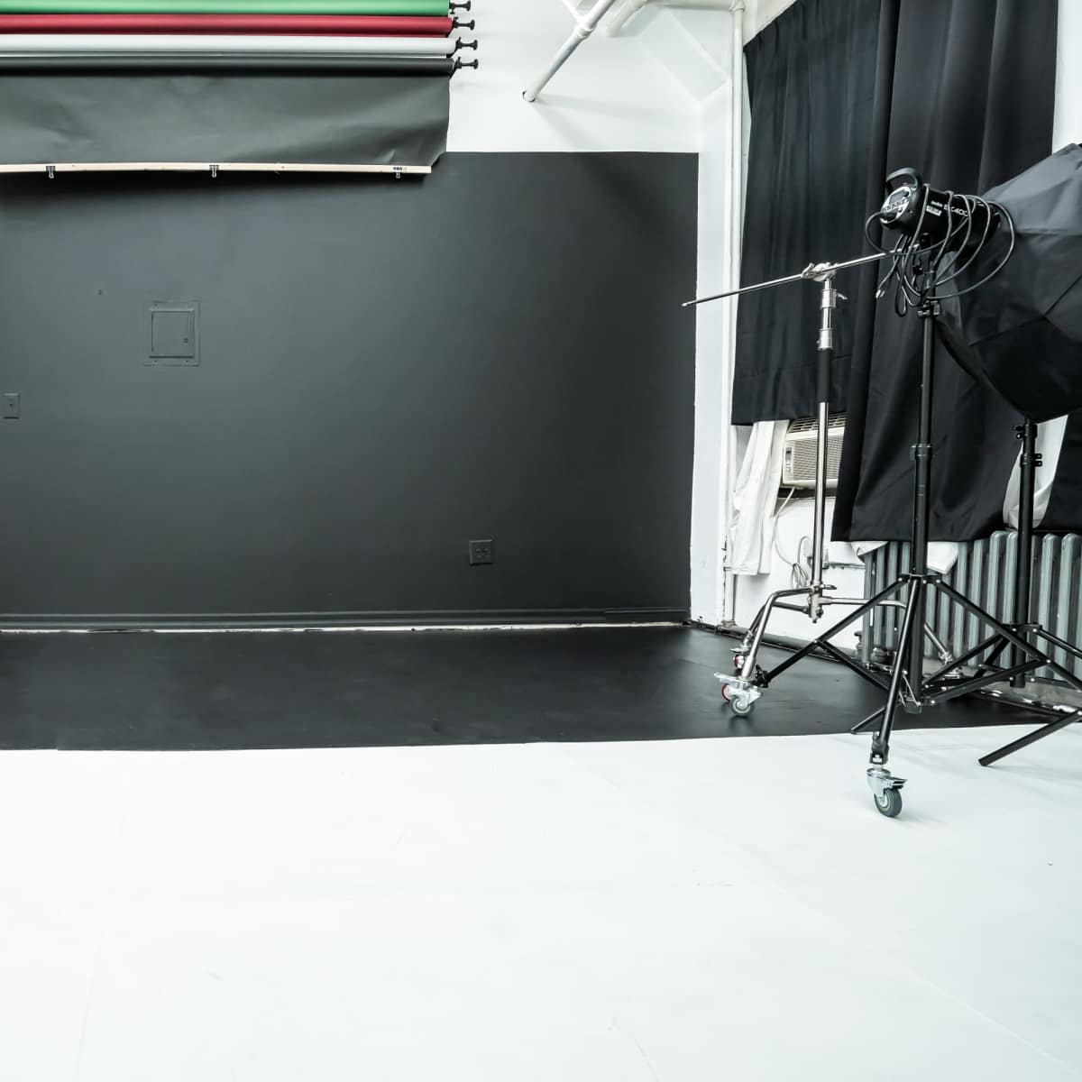 A photography studio with a black backdrop and a light stand on one side, along with a section of white floor.