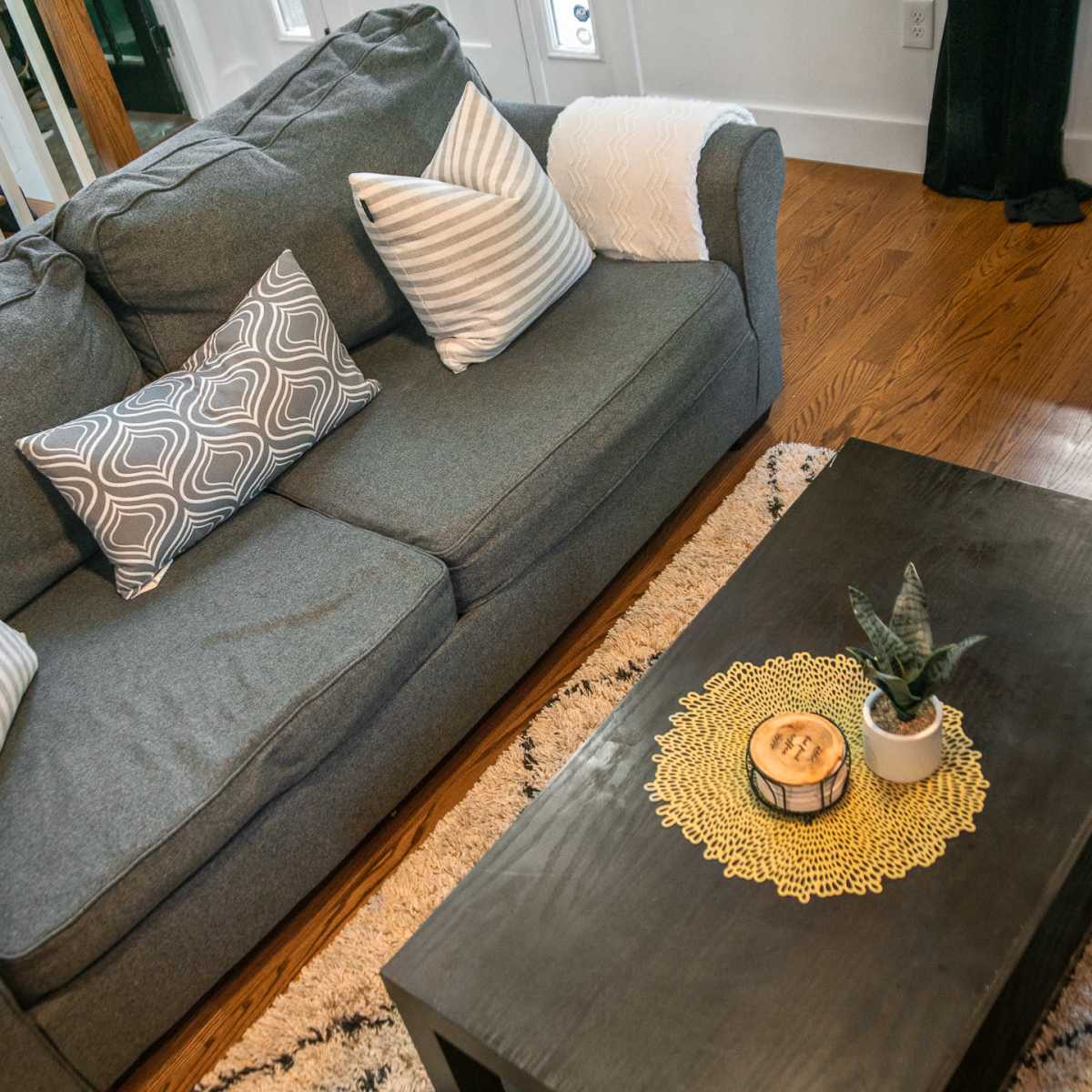 A gray sofa with patterned pillows sits in a living room, accompanied by a dark coffee table featuring a plant and a decorative tray.