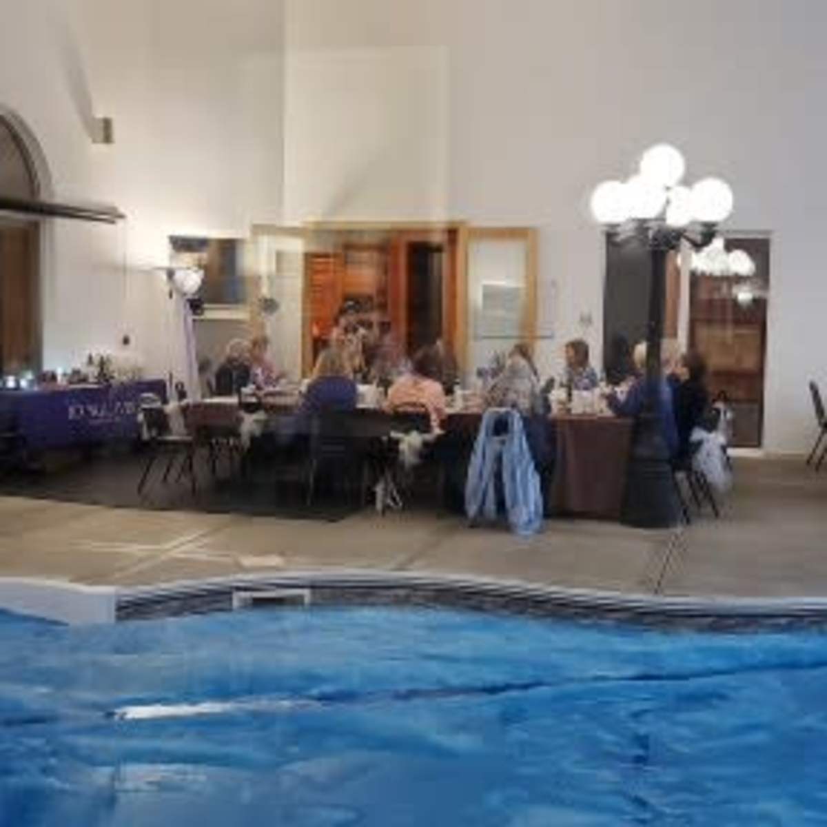 A group of people is gathered around a table in a dining area adjacent to a swimming pool.