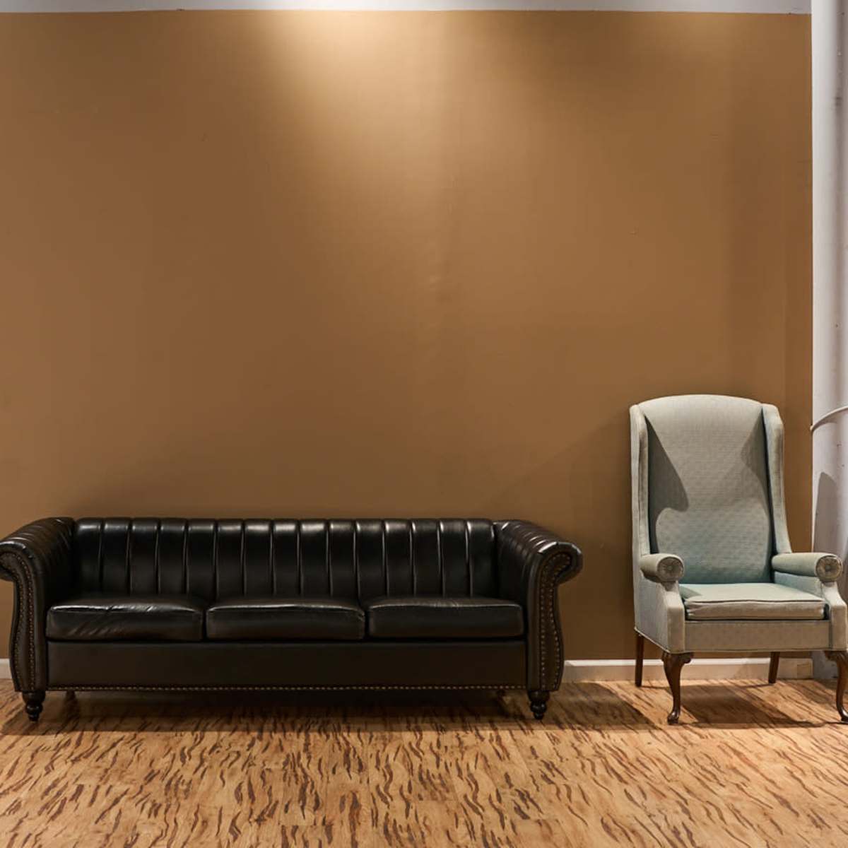 A black leather couch and a light blue upholstered armchair are positioned against a two-tone brown and green wall.