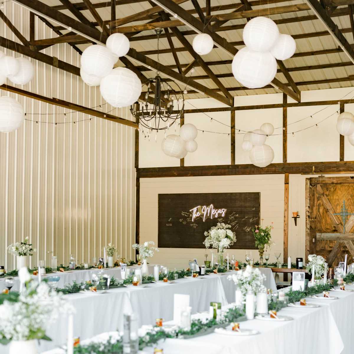 A large indoor event space with tables set for a gathering, decorated with white lanterns and floral arrangements.