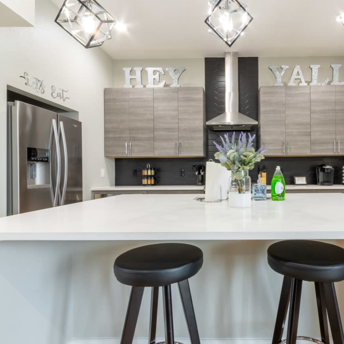 A modern kitchen with gray cabinets, a white countertop, and two black bar stools.