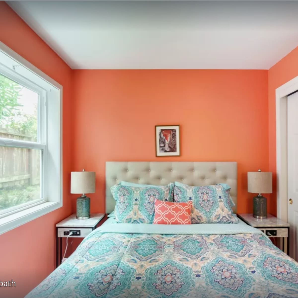 A bedroom with an orange wall, a bed covered in a patterned quilt, and two bedside tables with lamps on either side.