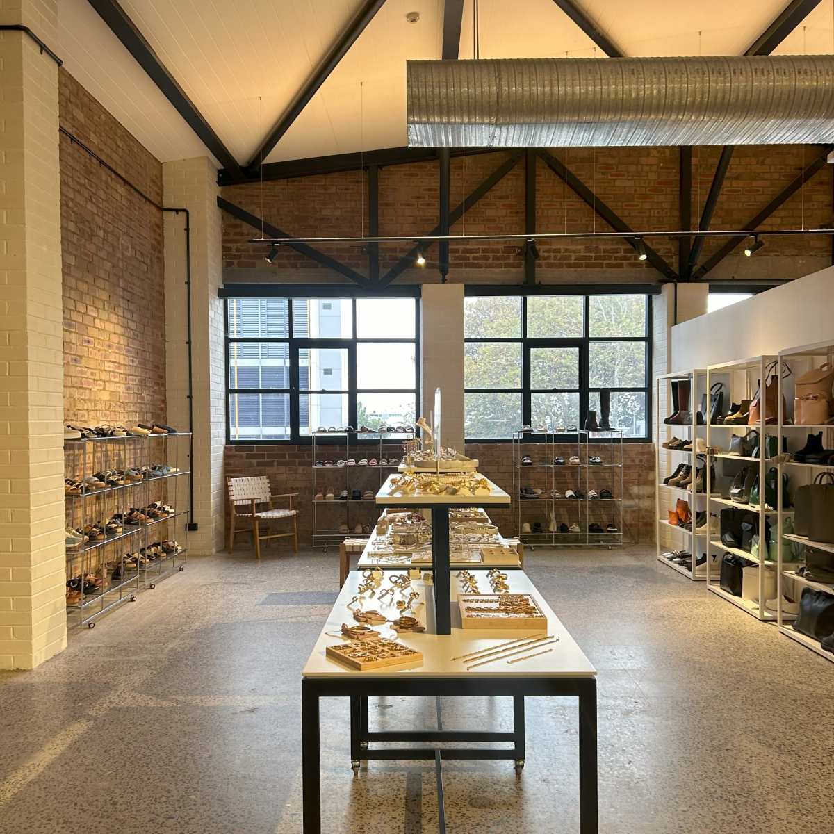 A retail store with a minimalist design, featuring shelves of shoes on one side and a table displaying accessories in the center, all within a brick-walled space.